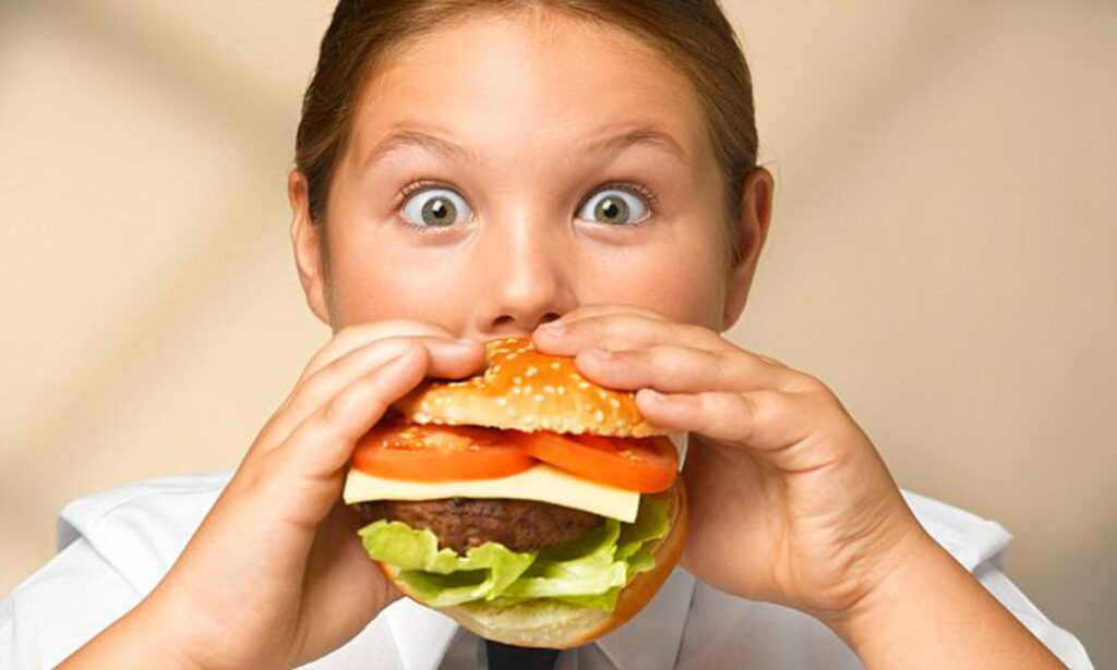 Criança come hambúrger recheado: como a ansiedade infantil afeta a fome das crianças?