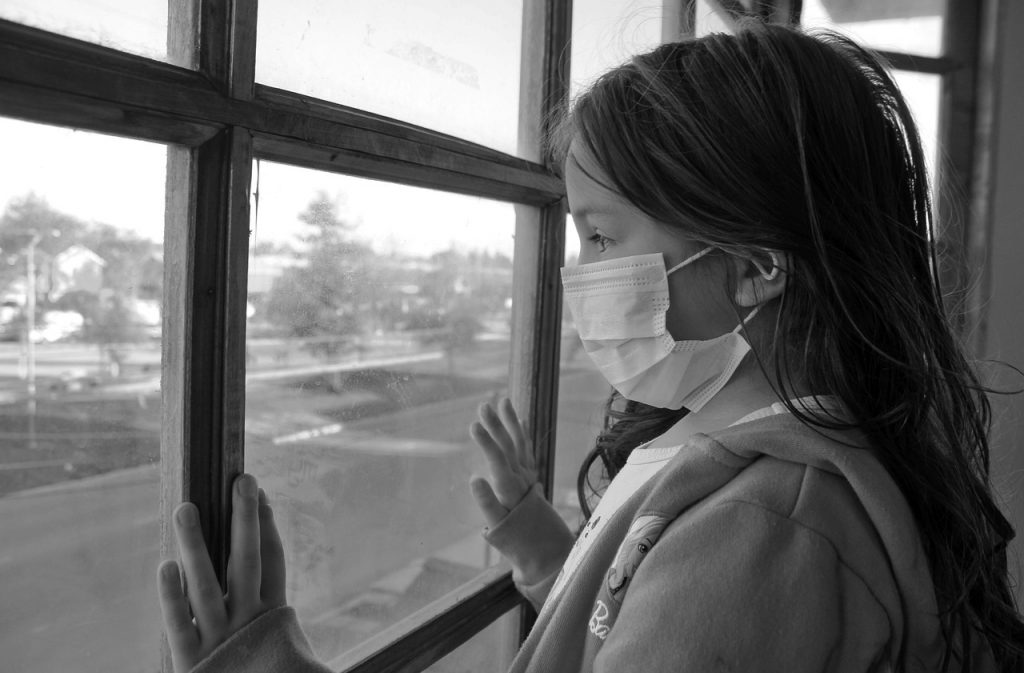 Criança protegida com máscara olha pela janela: pediatras devem estar atentos a todos os sinais da criança enferma