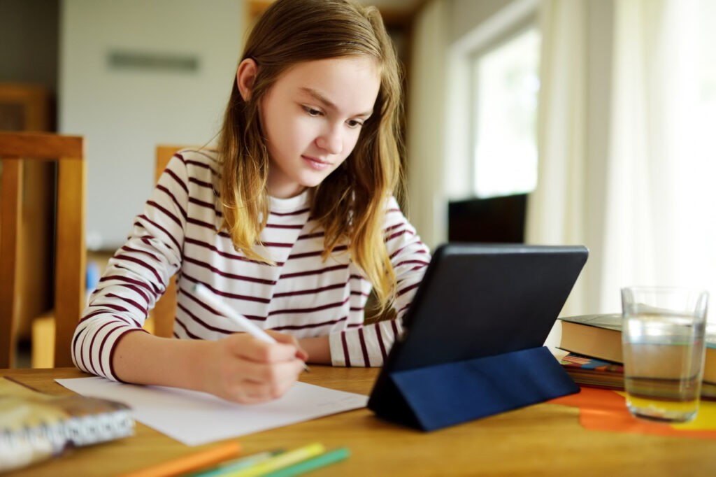 Menina realiza tarefa escolar olhando para um tablet: saiba como ajudar no aprendizado online das crianças