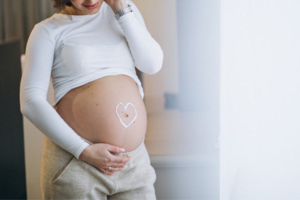 Gestante olha para a sua barriga durante a gravidez: muitas mulheres se perguntam: como cuidar da pele durante a gravidez?