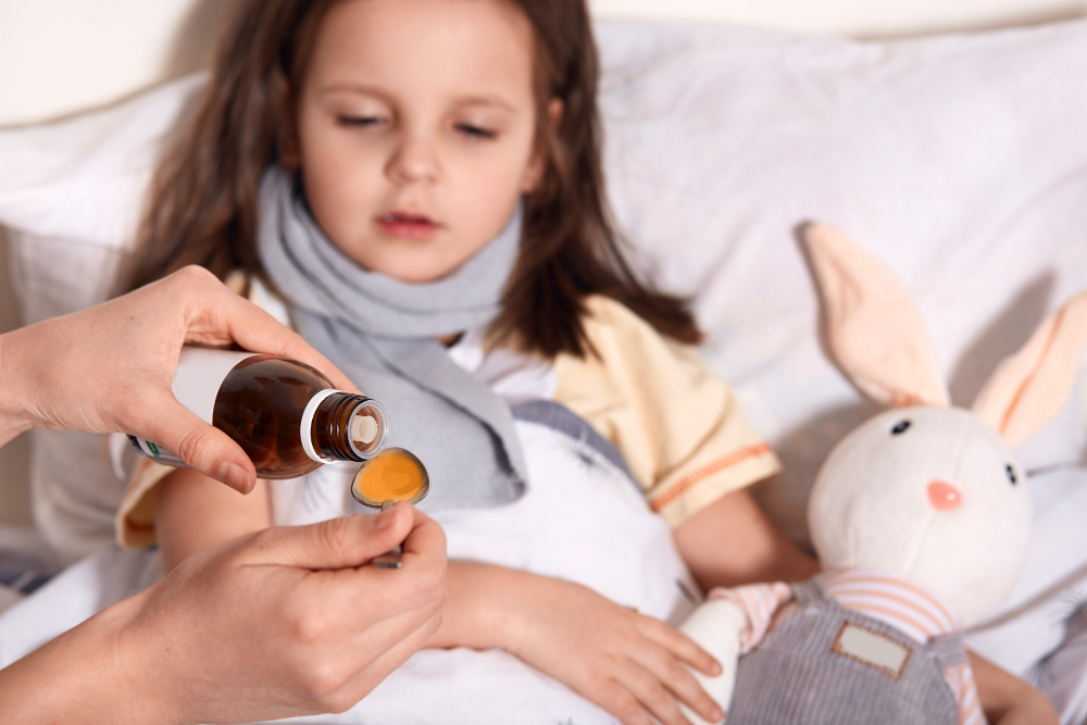 Criança observa remédio que irá tomar ao ser medicada por um adulto: a coqueluche é uma infecção contagiosa que atinge as vias respiratórias, que são responsáveis por levar o ar até os nossos pulmões.